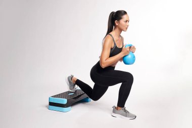 Asyalı bir kadın Kettlebell 'le çalışıyor. Beyaz arka planda spor kıyafeti giyiyor.,