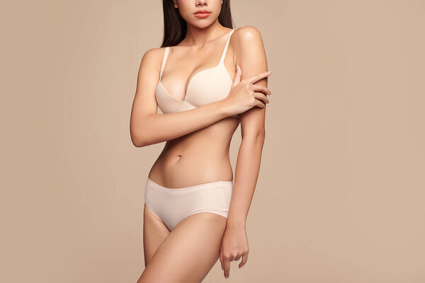 Уверенная в себе красивая молодая азиатская женщина позирует в белом белье на бежевом фоне, идеальное тело,