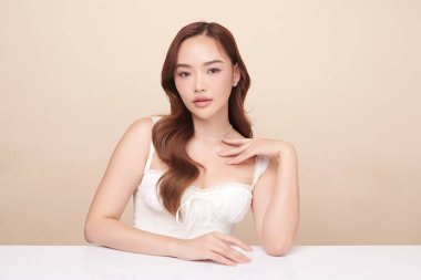 Güzel, genç bir Asyalı kadın, bej bir arka planda temiz, taze bir ten. Cilt bakımı, yüz bakımı, kozmetoloji, güzellik ve kaplıca. Asyalı bir kadının zarif bir portresi..
