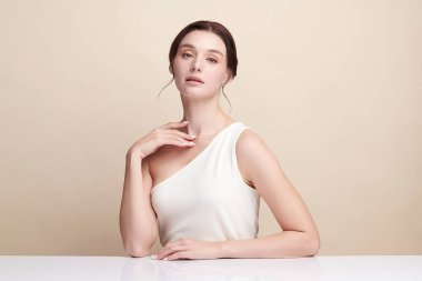 Bej bir arka planda temiz, taze bir teni olan güzel bir genç kadın. Cilt bakımı, yüz bakımı, kozmetoloji, güzellik ve kaplıca. Bir kadının zarif bir portresi..