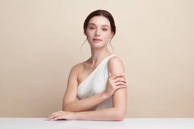 Bej bir arka planda temiz, taze bir teni olan güzel bir genç kadın. Cilt bakımı, yüz bakımı, kozmetoloji, güzellik ve kaplıca. Bir kadının zarif bir portresi..