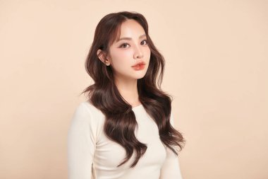 Güzel, genç bir Asyalı kadın, bej bir arka planda temiz, taze bir ten. Cilt bakımı, yüz bakımı, kozmetoloji, güzellik ve kaplıca. Asyalı bir kadının zarif bir portresi..