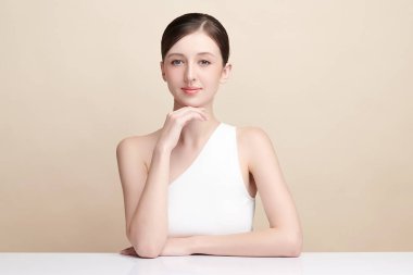 Bej bir arka planda temiz, taze bir teni olan güzel bir genç kadın. Cilt bakımı, yüz bakımı, kozmetoloji, güzellik ve kaplıca. Bir kadının zarif bir portresi..