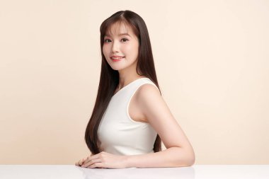 Güzel, genç bir Asyalı kadın, bej bir arka planda temiz, taze bir ten. Cilt bakımı, yüz bakımı, kozmetoloji, güzellik ve kaplıca. Asyalı bir kadının zarif bir portresi..