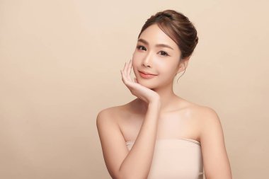 Güzel, genç bir Asyalı kadın, bej bir arka planda temiz, taze bir ten. Cilt bakımı, yüz bakımı, kozmetoloji, güzellik ve kaplıca. Asyalı bir kadının zarif bir portresi..