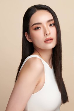 Güzel, genç bir Asyalı kadın, bej bir arka planda temiz, taze bir ten. Cilt bakımı, yüz bakımı, kozmetoloji, güzellik ve kaplıca. Asyalı bir kadının zarif bir portresi..