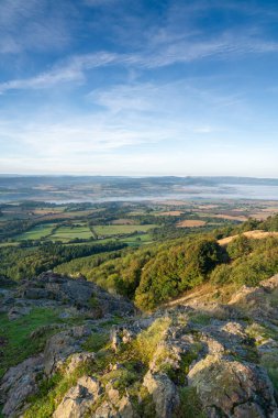 A view of misty countryside in Shropshire, UK with a rocky foreground  taken from the summit of the Wrekin hill in portrait orientation clipart