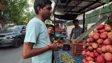 Şehirde taze liçi, kiraz ve kırmızı elma meyvesi satan bir adam var.