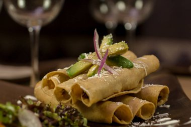 Crispy tacos dorados stuffed with beef and garnished with avocado slices and sour cream served over a clay plate. clipart