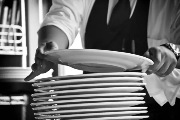 Garson restoran servisinde seramik tabakları üst üste yığıyor, tek renkli yakın plan..