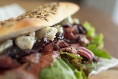 Zengin mavi peynirli İtalyan panini sandviçi, karamelli soğan, biftek ve marul, yakın plan..