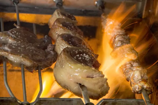 Biftekli üç Brezilya şişi, picanha, ve üst fileto profesyonel bir mutfakta alevler içinde yanıyor..