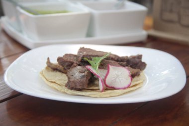 Taze mısır tortilla ızgara sığır filetosu, turp ve kişniş ile süslenmiş, beyaz seramik tabakta servis edilir..