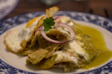 Serrano biber soslu, kızarmış yumurta ve parçalanmış peynirle kaplanmış canlı yeşil chilaquiles geleneksel Talavera tabağında servis edilir..