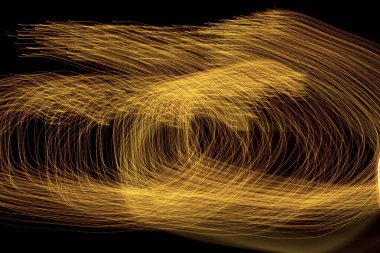 Soyut altın ışık yolları uzun pozlama ve kamera dönüşü yoluyla kaotik dairesel desenler oluşturarak parlayan bir yuvaya ya da girdap oluşturur..