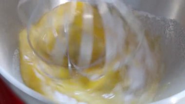Mixing raw eggs in a silver kitchen stand mixer. Whipping the eggs. Slow motion.