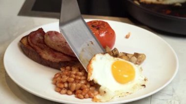 Tabakta İngiliz kahvaltısı. Bir aşçı kahvaltı tabağına fasulye, domuz pastırması ve tost ile kızarmış yumurta koyar. Yüksek kaliteli FullHD görüntüler