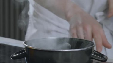 Mutfak işleri. Bir aşçı elektrikli ocaktan buharlı bir tencereyi çıkarır. Yüksek kalite 4k görüntü