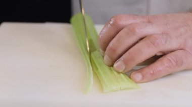 Aşçı kereviz saplarını büyük bir mutfak bıçağıyla küçük dilimlere ayırır. Mutfak masasında gri bir plastik tahta üzerinde kereviz doğrayan metal bıçak. Yüksek kalite 4k görüntü