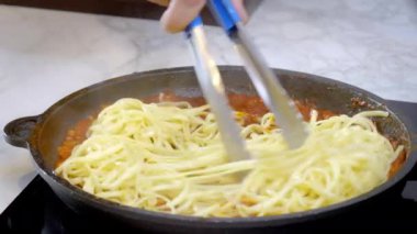 Yakın plan çekimde tavaya konan pişmiş spagetti ve sıcak kırmızı makarna sosuyla karıştırılıyor. Yüksek kalite 4k görüntü