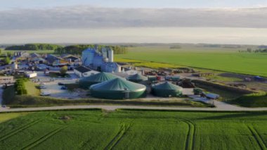 Anayoldan geçen geniş tarımsal arazili hava manzarası. Uzakta, biyogaz fabrikası, domuz çiftliği ve tahıl depolama konteynırları olan bir tarım üretim kompleksi. 4k görüntü