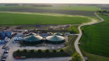 Anayoldan geçen geniş tarımsal arazili hava manzarası. Uzakta, biyogaz fabrikası, domuz çiftliği ve tahıl depolama konteynırları olan bir tarım üretim kompleksi.