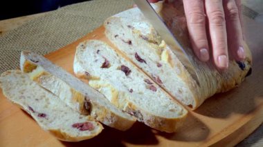 Zeytinli İtalyan ekmeği. Tahta kesme tahtasındaki ekmeği dilimlemek. Ekmek dilimleme bıçağıyla yakın plan..