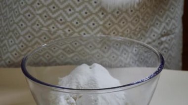 Yemek hazırlama. Bir aşçı hamur yapmak için elek ile un seçer. Seçilmiş un cam bir kaseye düşer..