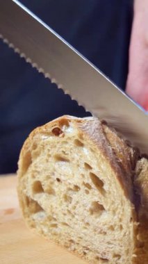 Ağır çekim. İtalyan ciabatta ekmeğini tahta bir tahtanın üzerinde ekmek bıçağıyla dilimlemek.