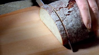 Tahta bir tahtanın üzerinde ekmek bıçağıyla siyah ekmeği dilimlemek. Yüksek kaliteli FullHD görüntüler