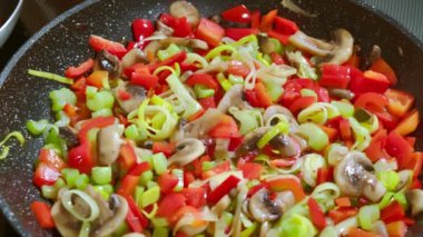 Yemek hazırlama. Yiyeceğe karabiber ekliyorum. Çeşitli sebzeler tavada kızarıyor, doğranmış sebzeler, kereviz sapları, pırasalar, mantarlar, kırmızı dolmalık biberler..