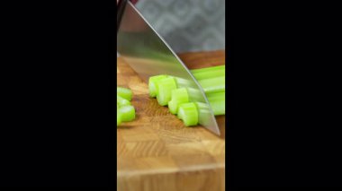 Dikey ekran video. Yemek hazırlama. Mutfak bıçağıyla aşçı ahşap tahtada kereviz sapı dilimliyor. Yiyeceklerle çalışmak için siyah lastik eldiven takan eller. Yüksek kalite 4k görüntü
