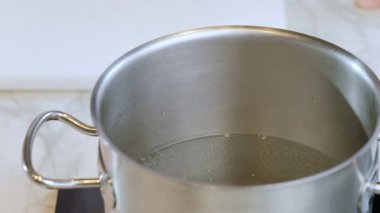 Yemek hazırlama. Sobanın üstünde bir tencere sıcak su. Aşçı tencereye tuz döker. Yavaş çekim videosu, seçici odak.