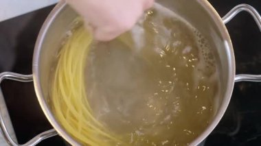 Yemek hazırlama. Spagetti tencerede kaynıyor ve aşçı onu tahta kaşıkla karıştırıyor..