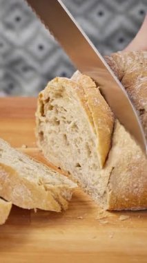 Dikey görüntü. Tahtada ekmek bıçağıyla ciabatta ekmeği dilimlemek..