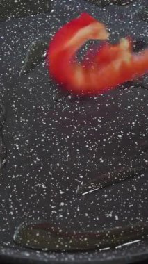 Dikey video. Aşçı tavaya kırmızı biber döker. Dolmalık biberi kızartıyorum..