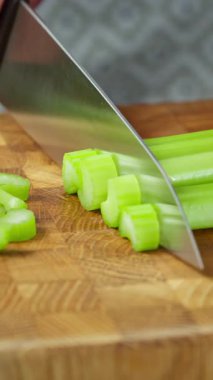 Dikey video. Mutfak bıçağıyla aşçı ahşap tahtada kereviz sapı keser..