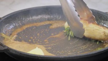 Kızarmış tavuk filetosu. Bir aşçı tavuk filetosunu sıcak tereyağı ve baharatla tavaya koymak için metal maşa kullanır. Yüksek kalite 4k görüntü