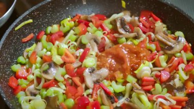Tavada kızartılan sebzelere domates sosu ekliyorum. Mantar, biber, pırasa, kereviz sapları tavada pişirilir. Yavaş çekim videosu. Yüksek kaliteli FullHD görüntüler