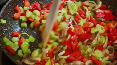  Bir aşçı ahşap bir spatulayla tavada kızartılan sebzeleri karıştırır. Mantar, biber, pırasa, kereviz sapları tavada pişirilir. Yavaş çekim videosu 100fps