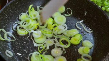 Bir şef, zeytinyağıyla tavada kızarırken tahta bir spatulayla dilimlenmiş pırasa karıştırır. Yavaş çekim videosu 100fps. Yüksek kaliteli FullHD görüntüler
