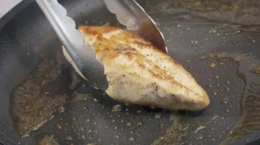 Yemek hazırlama. Sıcak zeytinyağının içinde tavada kızartılmış tavuk filetosu. Bir şef tavuk filetosunu metal maşayla kızartıyor. Yavaş çekim videosu 100fps. Yüksek kalite 4k görüntü