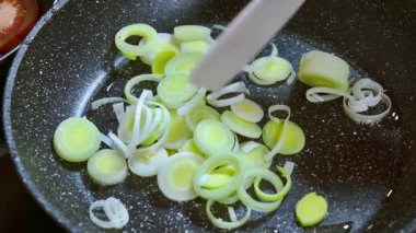 Bir şef, zeytinyağıyla tavada kızarırken tahta bir spatulayla dilimlenmiş pırasa karıştırır. Yavaş çekim videosu 100fps. Yüksek kaliteli FullHD görüntüler