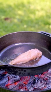 Dikey ekran görüntüleri. Bir şef, tavuk filetosunu ızgara kömürlerinde ısıtılan dökme demir bir tavaya koymak için metal maşa kullanır. Yemek hazırlama. Yüksek kaliteli FullHD görüntüler