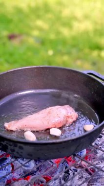 Dikey video. Açık hava ızgarasında sarımsaklı zeytinyağıyla kızartılan sulu bir parça tavuk filetosu, dökme demir bir tavada. Yavaş çekim 100 fp. Yüksek kaliteli FullHD görüntüler