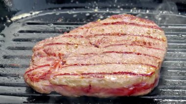 Yemek hazırlama. Dökme demir bir tavada pişmiş çiğ biftek. Şef bifteğe biber ekler. Yüksek kaliteli FullHD görüntüler