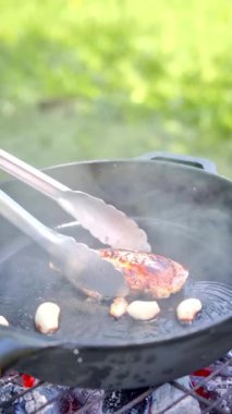 Dikey görüntü. Tavuk fileto bifteği, dışarıdaki mangal ızgarasında, sarımsak ve zeytinyağında, dökme demir bir tavada pişiriliyor. Tavadan kalın buhar yükseliyor. Yüksek kaliteli FullHD görüntüler