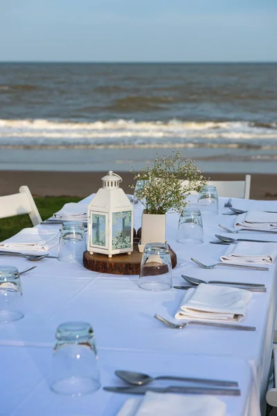 Table dinner set ready for an outdoor party near the beach. White tone decoration with white wooden chairs set.