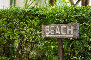 Plaj tabelası, tropik bir tatil köyünde beyaz harflerle ahşap bir tabağa boyanmış..