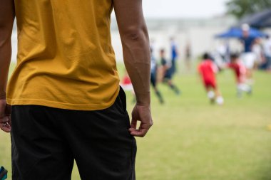 Baba, oğlunun güneşli bir günde bir okul turnuvasındaki futbol maçını seyrediyor. Spor, açık hava etkinliği, yaşam tarzı, mutlu aile ve futbol annesi ve futbolcu baba kavramı..